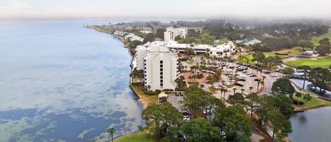 Vue aérienne d’un hôtel situé sur la côte, composé de plusieurs bâtiments, avec un terrain de golf et un port de plaisance.