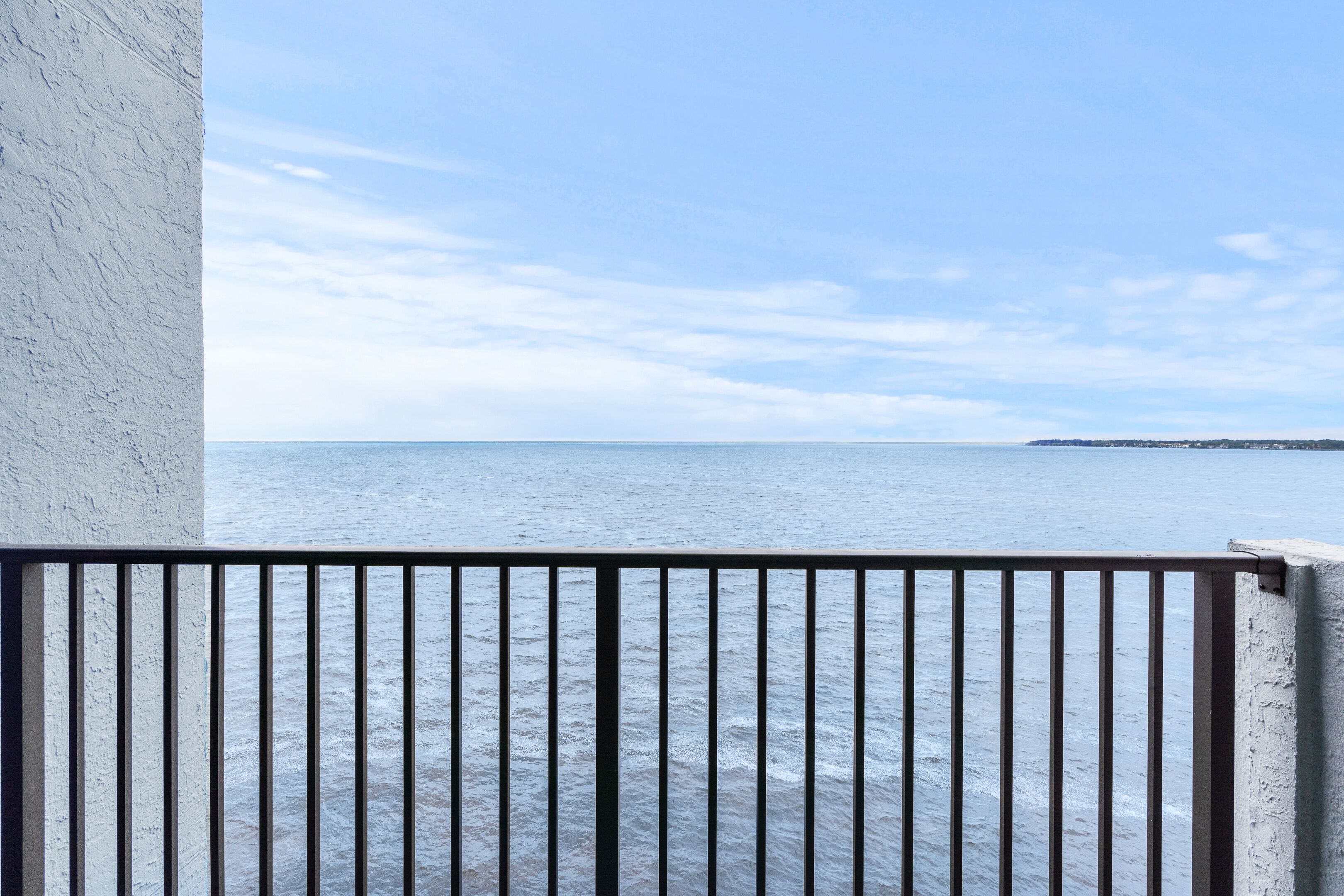 A balcony with a view of the sea and a distant shoreline.