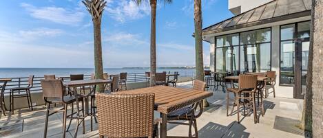An outdoor patio with wicker furniture, palm trees, and a view of the ocean.