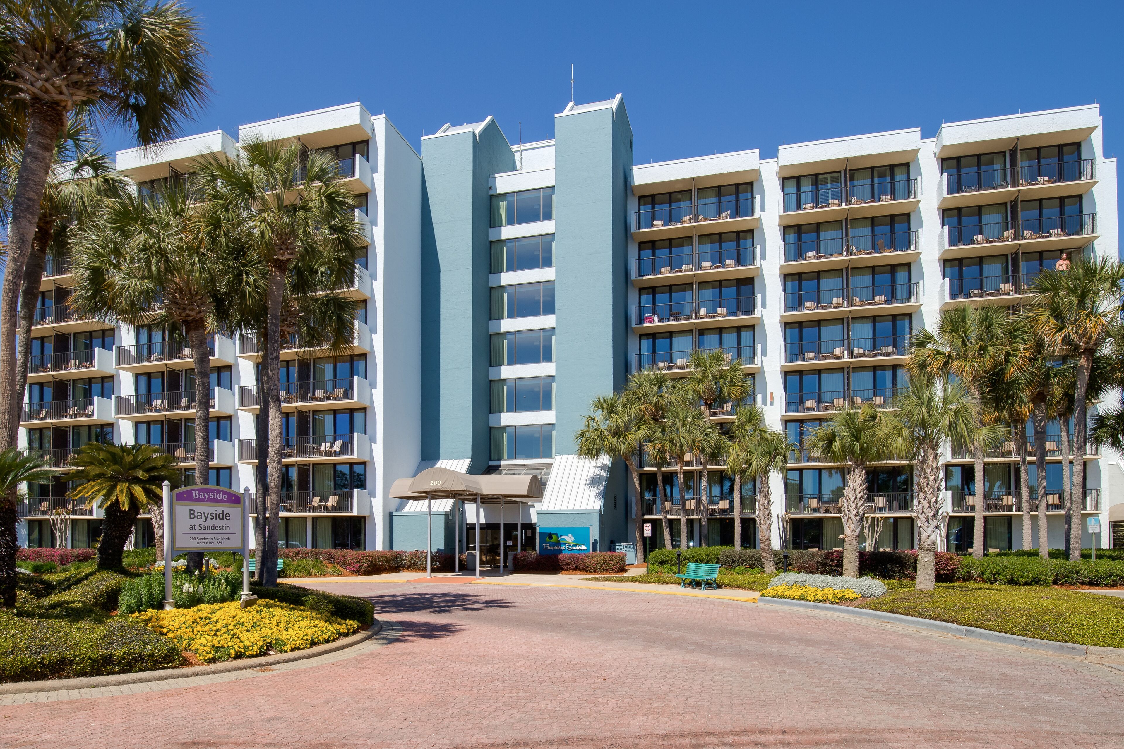 A multi-story hotel with a modern design, featuring balconies with outdoor seating and a landscaped entrance.