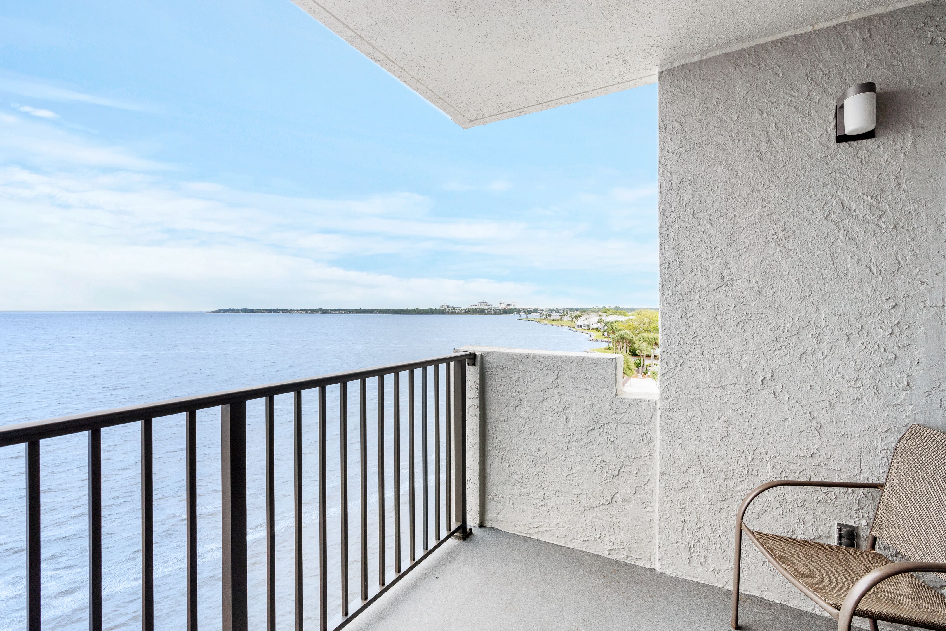 Un balcon avec vue sur la mer, une chaise et un mur à la texture particulière.