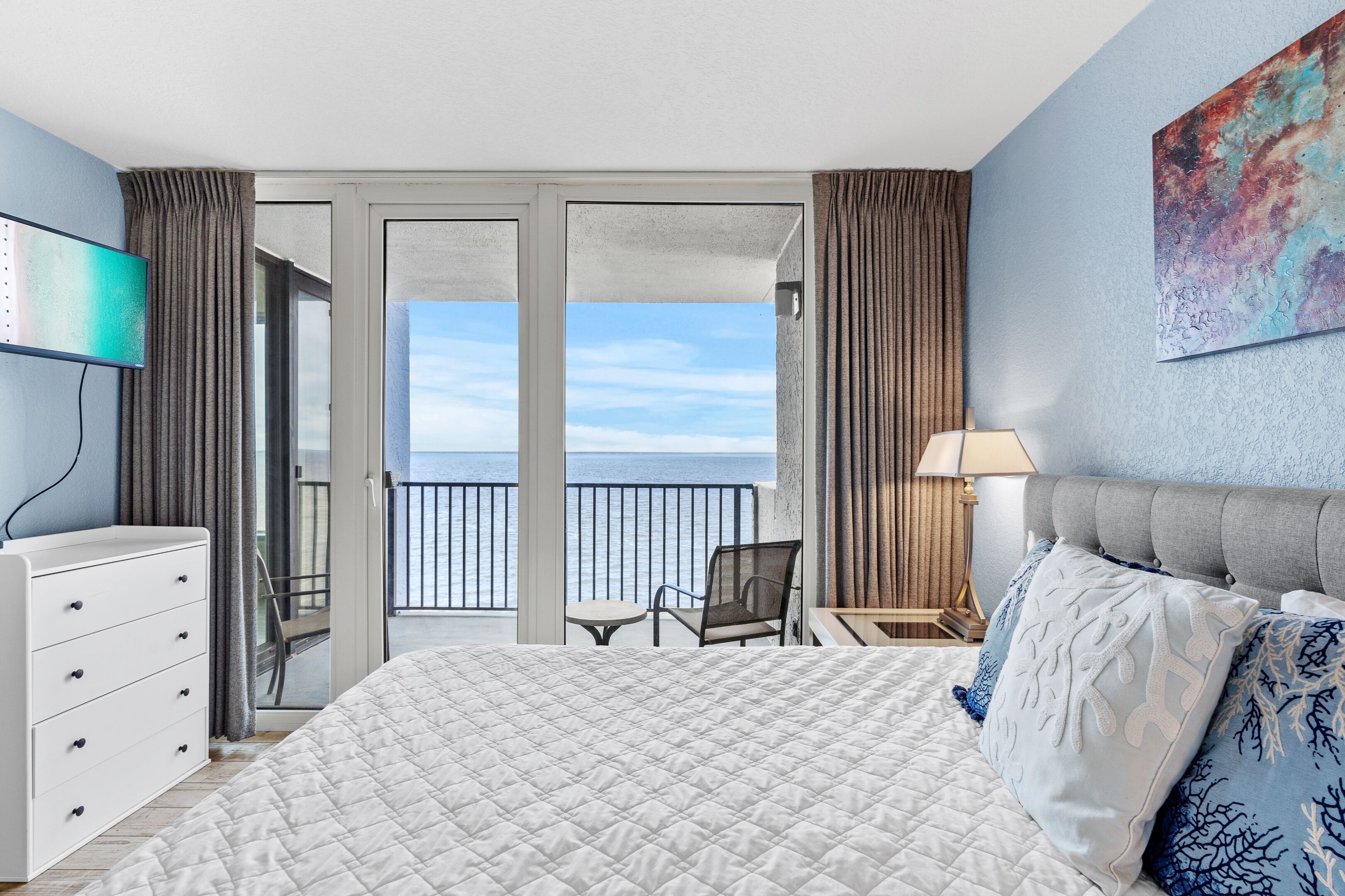 Habitación de hotel con cama, escritorio, silla, televisión y balcón con vistas al mar.