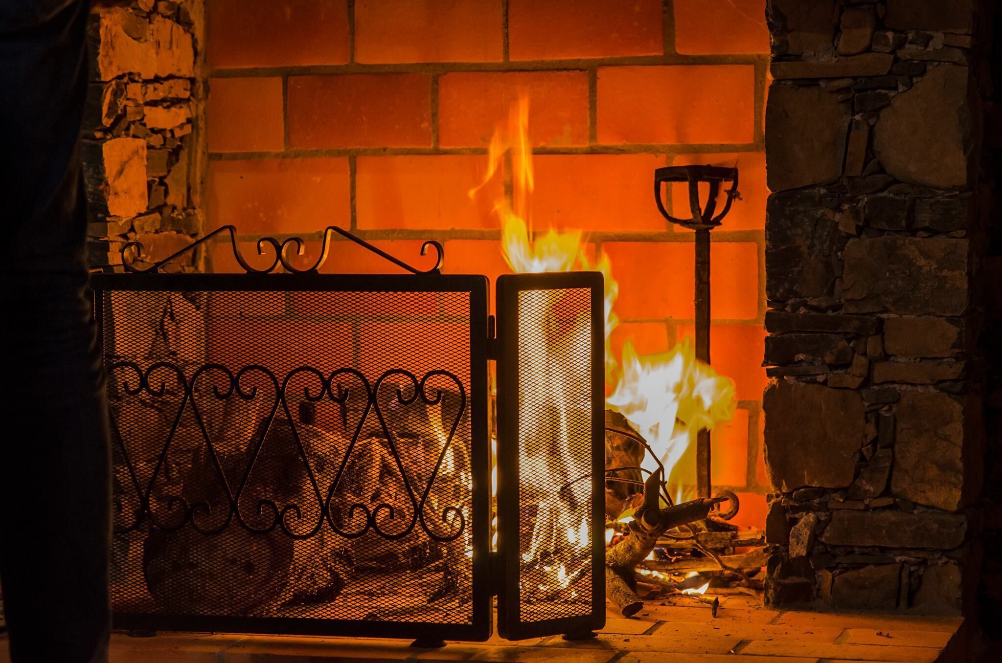 Ein Kamin mit Feuer, ein Metallsieb und eine Steinwand.
