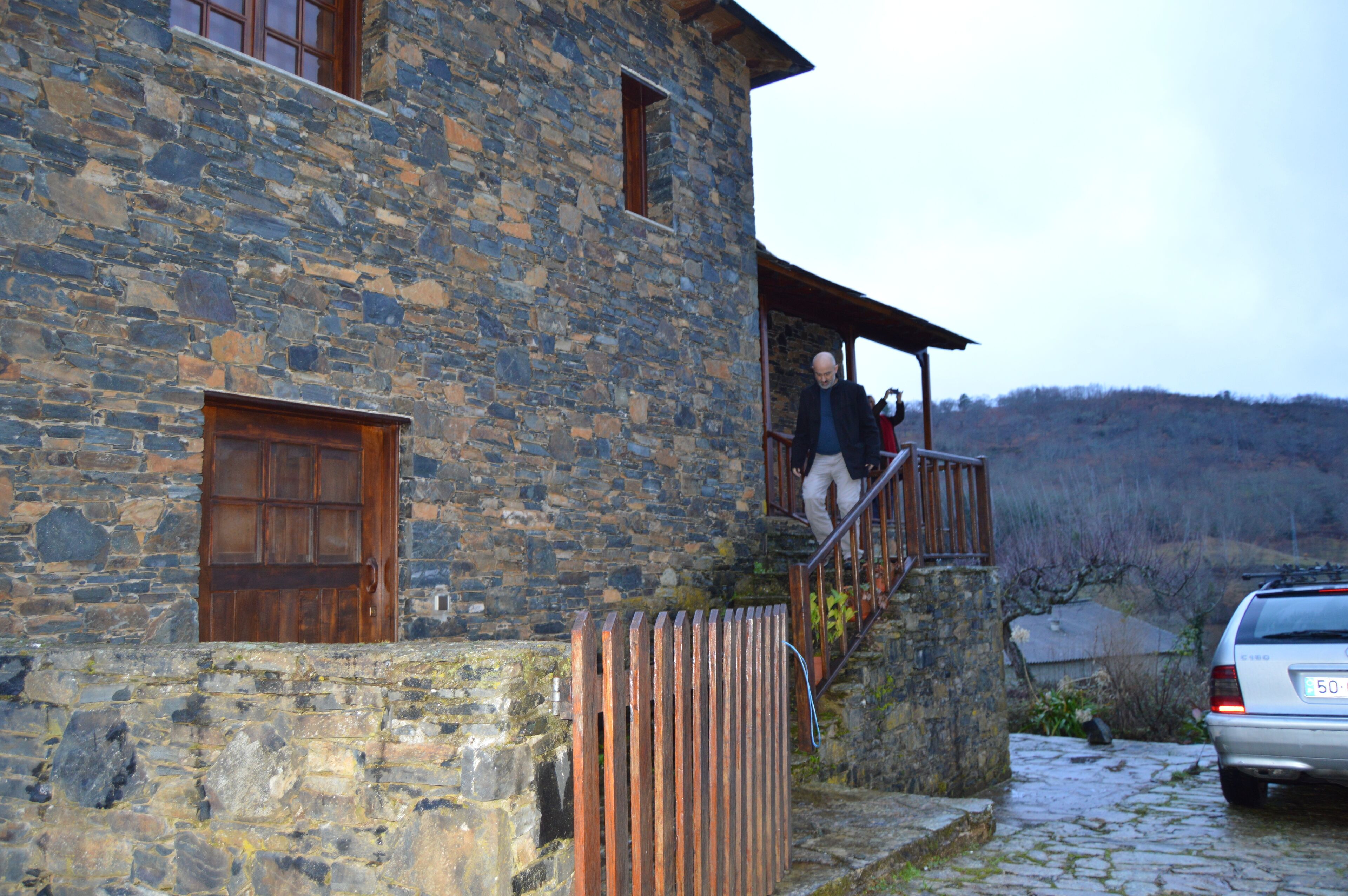 Un bâtiment en pierre avec une porte en bois et un escalier menant à une zone abritée.