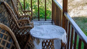 Een balkon met rieten stoelen en een tafel, met uitzicht op een bergachtig landschap.