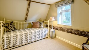 Une chambre avec un plafond en pente, un lit recouvert d’une literie à motifs, une lampe de chevet et une fenêtre donnant sur un paysage verdoyant.