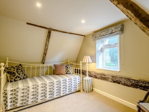 A bedroom with a sloped ceiling, a bed with patterned bedding, a bedside lamp, and a window with a view of greenery.