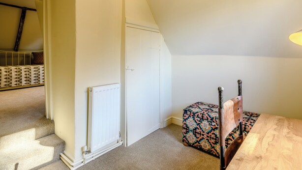 Une pièce avec un plafond en pente, un radiateur, un pouf à motifs et une table en bois avec une chaise.