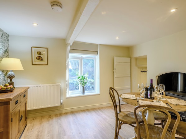 A well-lit kitchen with a dining table, chairs, a radiator, a window with a view, and a fireplace.