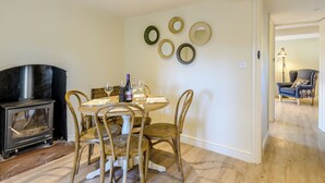 Un coin repas avec une table ronde, des chaises en bois, un petit poêle noir et des miroirs fixés au mur.
