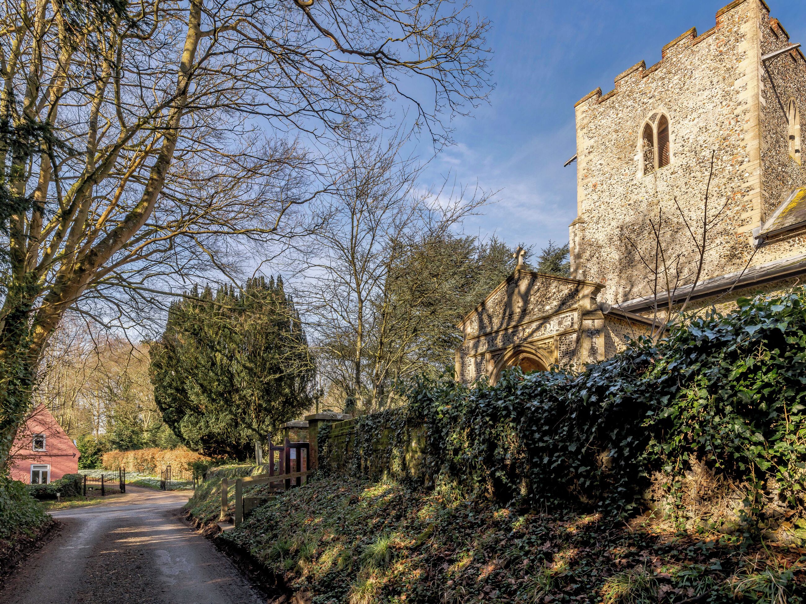 A rural road leading to a stone building with a tower, surrounded by trees and vegetation.