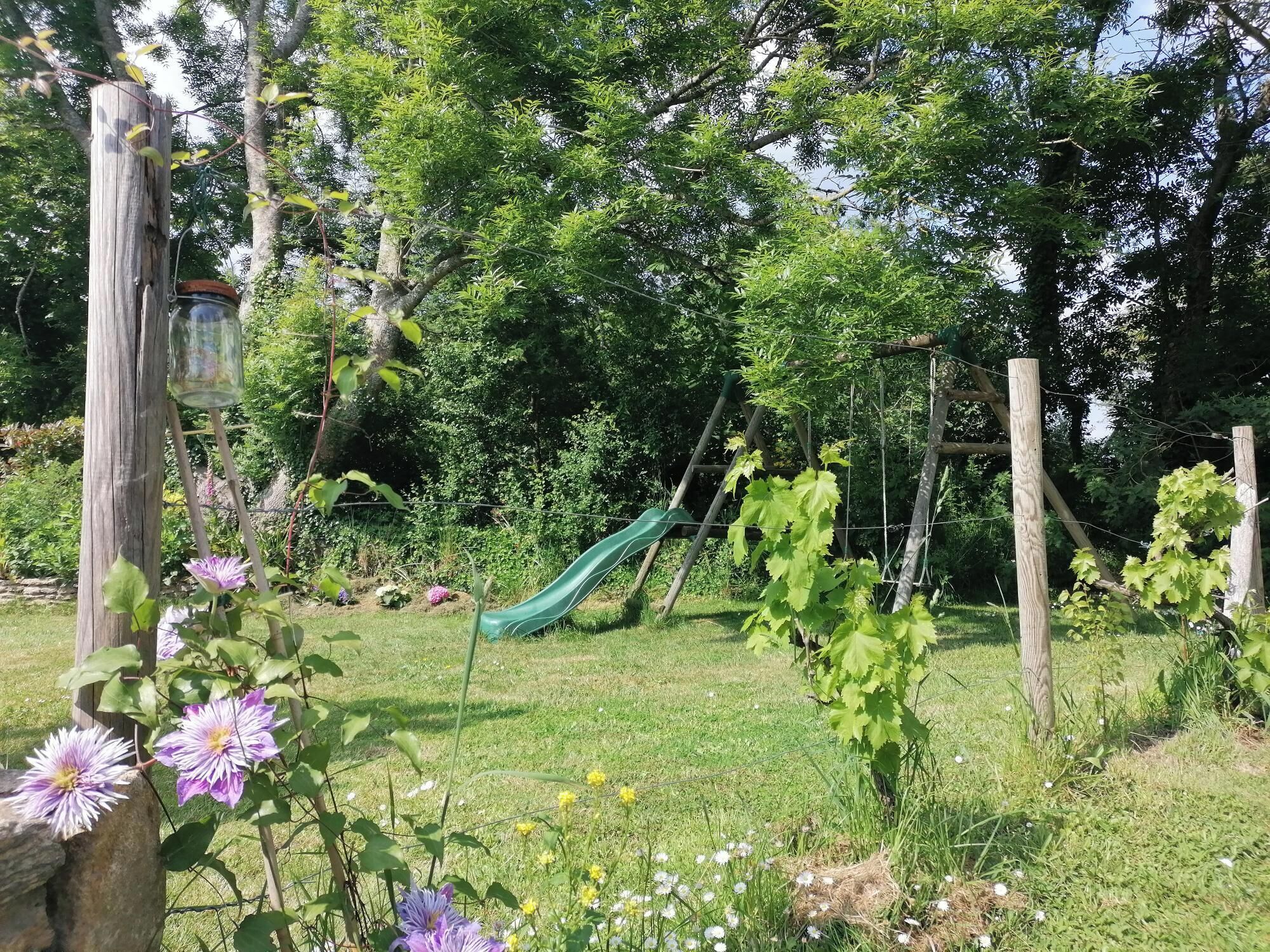 A garden with a wooden fence, a green slide, and various plants.