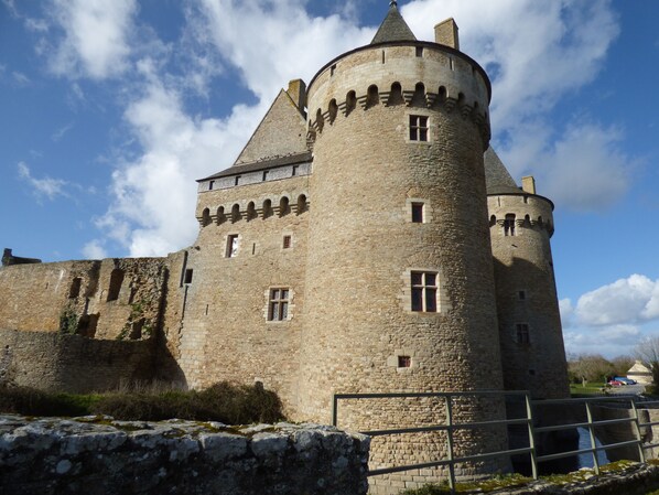 A historic stone castle with a round tower, large windows, and a fortified wall.
