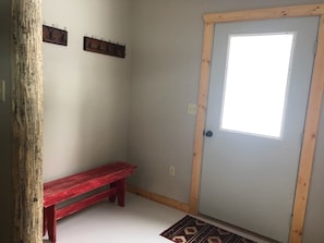 Een kamer met een houten deur, een bankje en twee haken aan de muur.