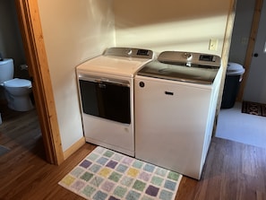 Een kleine wasruimte met een voorlader wasmachine en droger, houten vloeren en een kleurrijk vloerkleed.