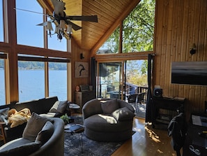 Een gezellig chalet met een groot raam met uitzicht op een meer, een comfortabele zithoek en een open haard.