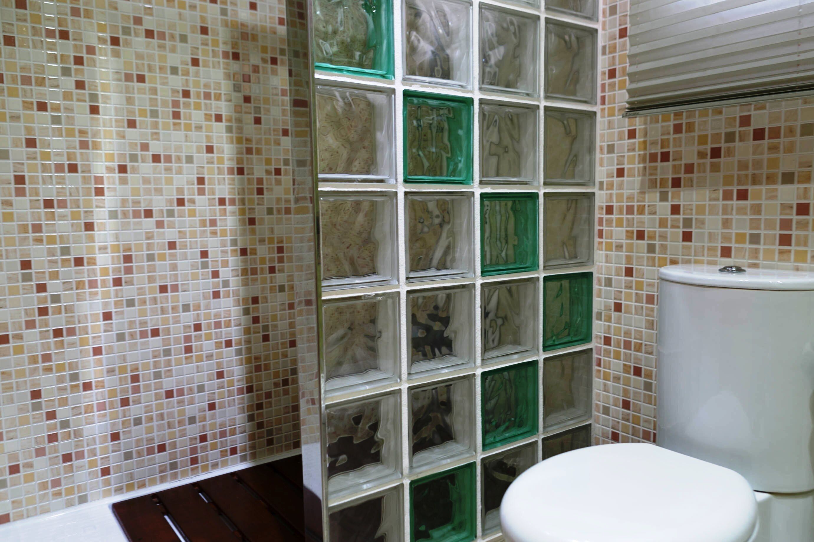 A bathroom with a tiled wall, a toilet, and a shower area.