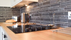 A modern kitchen with a black brick backsplash, a stainless steel kettle, a toaster, and a loaf of bread on the counter.