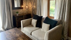Ein gemütliches Wohnzimmer mit einer Couch, einem Beistelltisch, einer Lampe und einem Fenster mit Vorhängen.