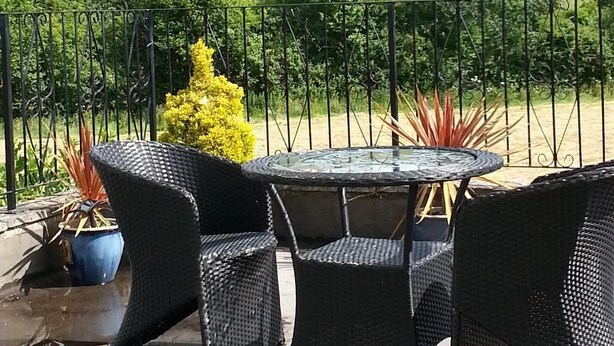Eine Terrasse im Freien mit Korbmöbeln und einem Glastisch, mit Blick auf eine grüne Landschaft.