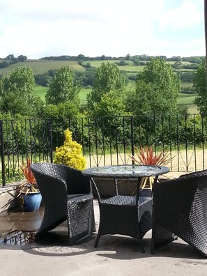 An outdoor patio with wicker furniture and a glass table, overlooking a green landscape. - Cosy First Floor rural Apartment with Views (Wells)