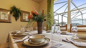 A dining table set for four with clear glassware, plates, and a centerpiece of red flowers. - Blue Jay Villa - Vacation Home Near Disney (Davenport)