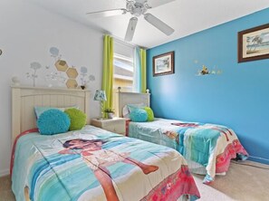 Une chambre avec deux lits, un ventilateur de plafond et un mur bleu orné d’un tableau encadré.