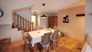 Een eetgedeelte met een houten tafel en stoelen, een trap en een klok aan de muur.