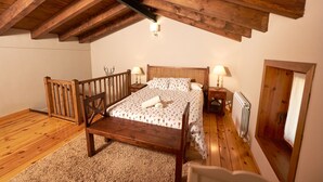 Een slaapkamer met een houten plafond, een bed met bloemenbedekking, twee nachtlampjes en een radiator.