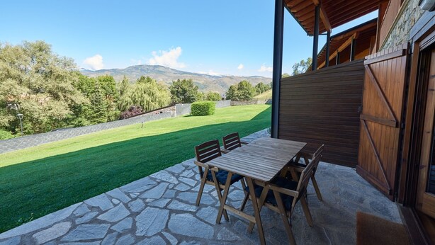 Een terras met een tafel en stoelen, een stenen vloer en uitzicht op een groen gazon en bergen.