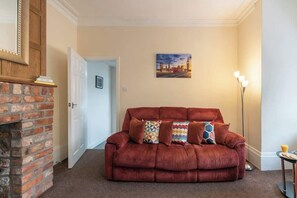 Un salon avec un canapé rouge, une cheminée en briques, une porte et un tableau accroché au mur.