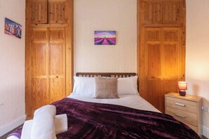 Une chambre à coucher avec un lit, une armoire en bois, une table de chevet et un tableau accroché au mur.