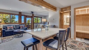 A modern living room with a large island table, dark blue sofa, and a patterned rug. - 🏔️Ski Access~Hot Tub~Studio Premier 106🏔️ (Snowmass Village)