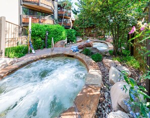 Relax in a serene hot spring area surrounded by lush greenery and natural rock formations.