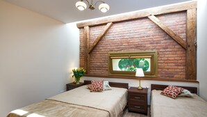 A bedroom with two beds, a brick wall, a window with a view, and a chandelier. - KrakowRentals - Vanilla 7 Apartment (Kraków)