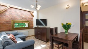 A living room with a brick wall, a flat-screen TV, a dining table with chairs, a sofa, and a vase with flowers. - KrakowRentals - Vanilla 7 Apartment (Kraków)