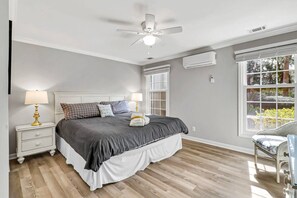 Una camera da letto con un letto, comodini, una ventola a soffitto, un condizionatore d'aria e una finestra con persiane.