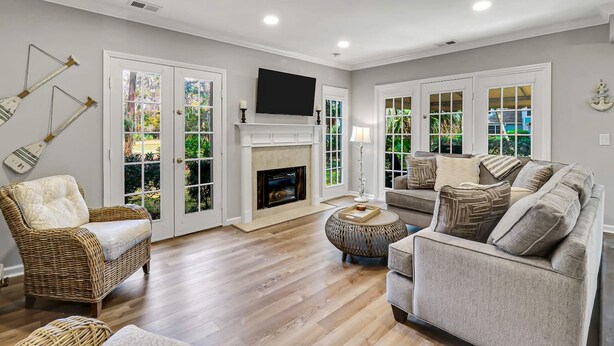 Una sala de estar con chimenea, televisor, muebles de mimbre y ventanas grandes con vistas al follaje.
