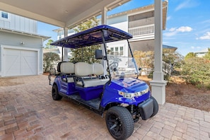 A blue golf cart parked on a brick driveway in front of a house with a covered porch.