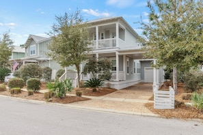 A two-story house with a porch, a garage, and a well-maintained front yard with various shrubs and a small tree.