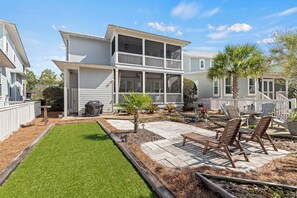 A two-story house with a balcony, a patio with chairs, and a well-maintained lawn.