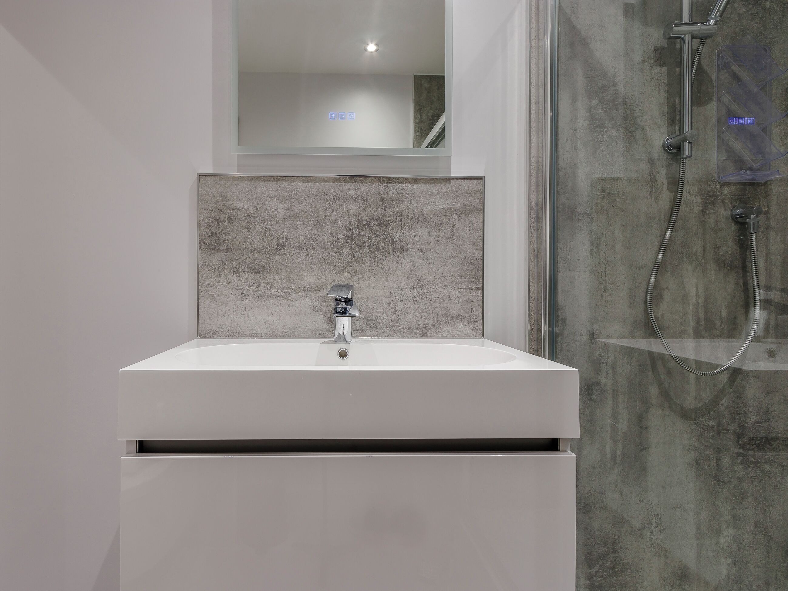 Een moderne badkamer met een witte wastafel, een spiegel erboven en een douche met een glazen deur.