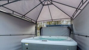 Un bain à remous installé sous une tente dotée d’une structure métallique et posée sur un sol herbeux.