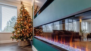 Un salon moderne avec un grand sapin de Noël, une cheminée et une vue sur l’extérieur.