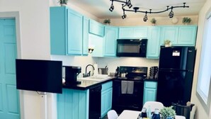 Une cuisine moderne avec des meubles de couleur turquoise, un réfrigérateur noir, un four à micro-ondes et un coin repas comprenant une table et des chaises blanches.