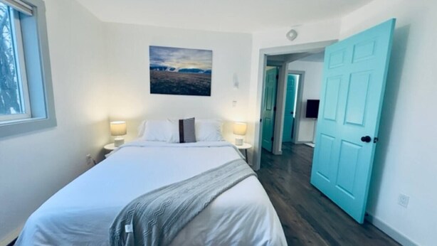 Une chambre à coucher avec un lit, un tableau accroché au mur et une porte donnant sur une autre pièce.