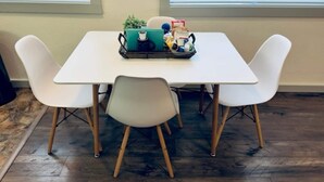 Un coin repas avec une table blanche et quatre chaises blanches. Un plateau vert contenant divers objets est posé sur la table.