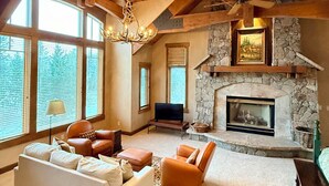 A spacious living room with a stone fireplace, large windows, and a high ceiling with exposed beams. - Stunning custom Home w/ private hot tub, quick drive to the slopes! (Keystone)