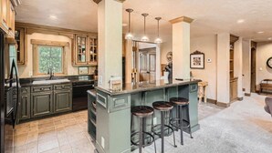 A spacious kitchen with a large island, bar stools, and a view of the dining area. - Stunning custom Home w/ private hot tub, quick drive to the slopes! (Keystone)