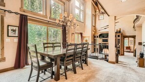 A spacious dining area with a large wooden table and chairs, surrounded by large windows offering a view of the outdoors. - Stunning custom Home w/ private hot tub, quick drive to the slopes! (Keystone)